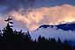 Sunset light on storm clouds over coastal mountain peak and forest, above Howe Sound, Sea-to-Sky Road, near Squamish, British Columbia, Canada