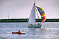 Sailboat passing Lone male adult person fishing from kayak in harbor channel, Newport Beach, Orange County, Southern California Coast