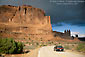 Picture: Car on two lane road belwo red rock cliffs, Arches National Park, Utah