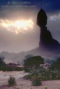 Sunburst through misty morning storm clouds next to Balanced Rock, Arches National Park, Utah